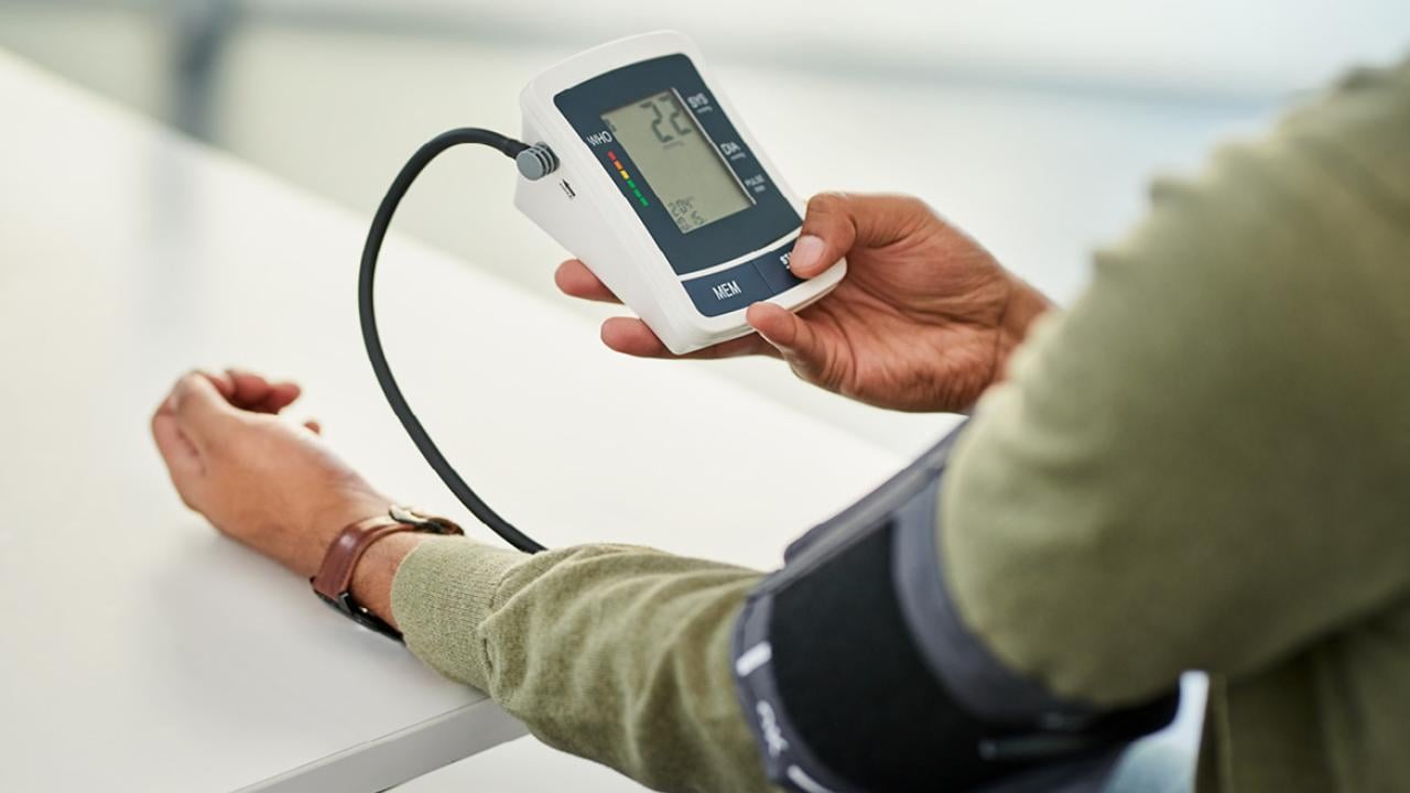 Person with an arm pressure cuff holding a blood pressure monitor. Tight shot.