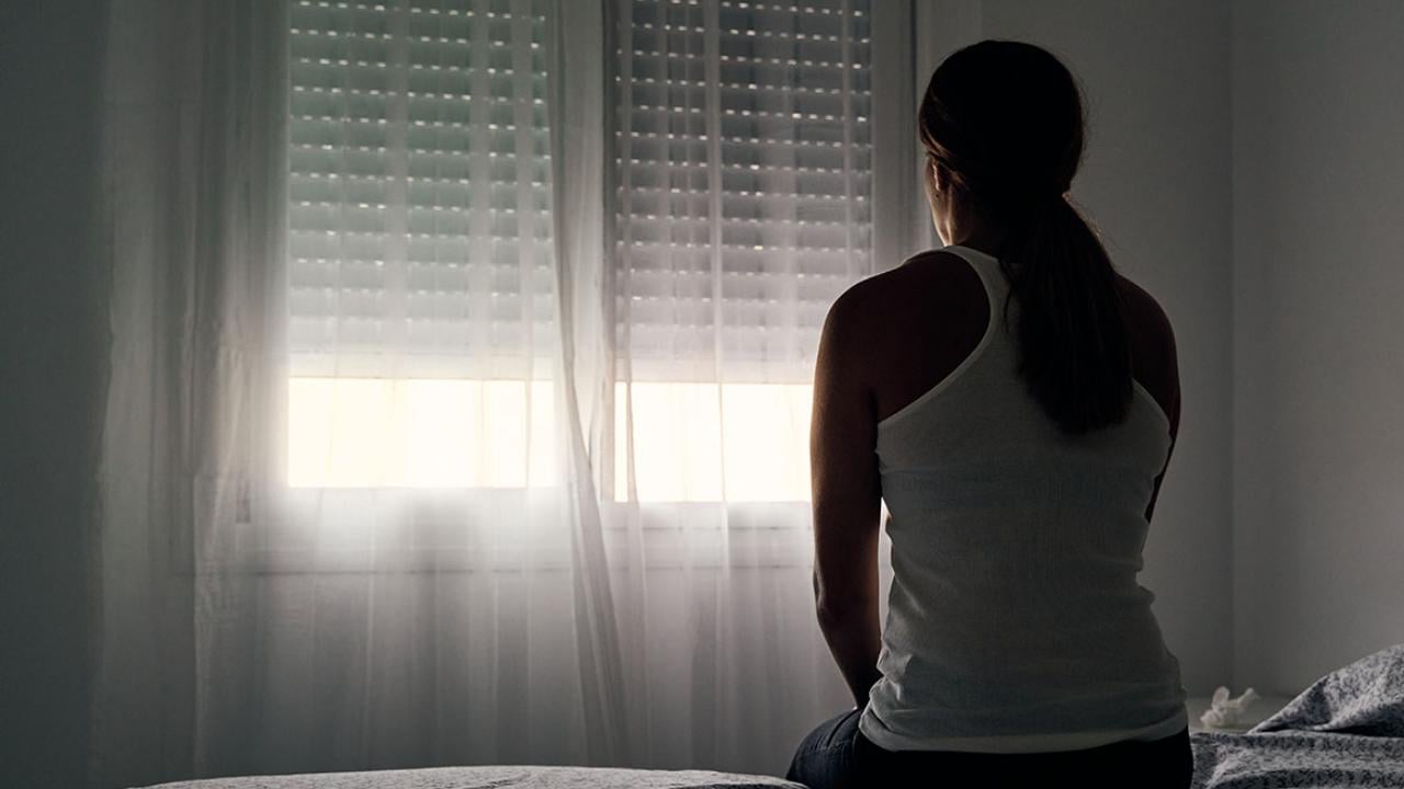 Rear view of woman sitting on a bed looking out the window