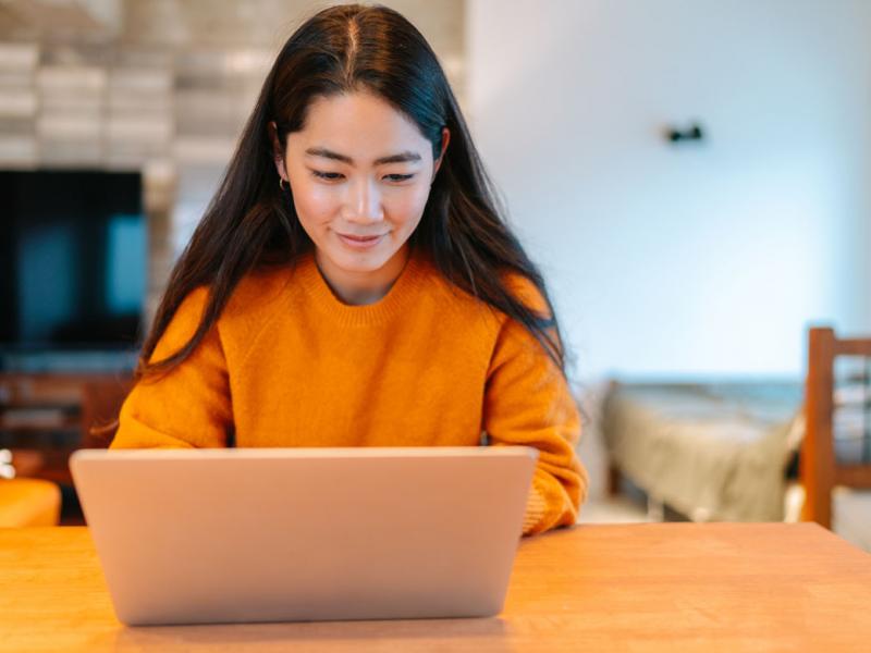 Woman smiling, working at her lap top in her living room.