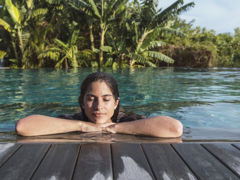 Woman with eyes closed at a tropical resort with palm trees in background