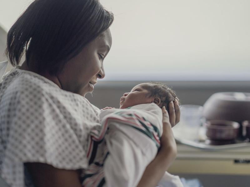 A mother holds her newborn baby as she sits up in a hospital bed