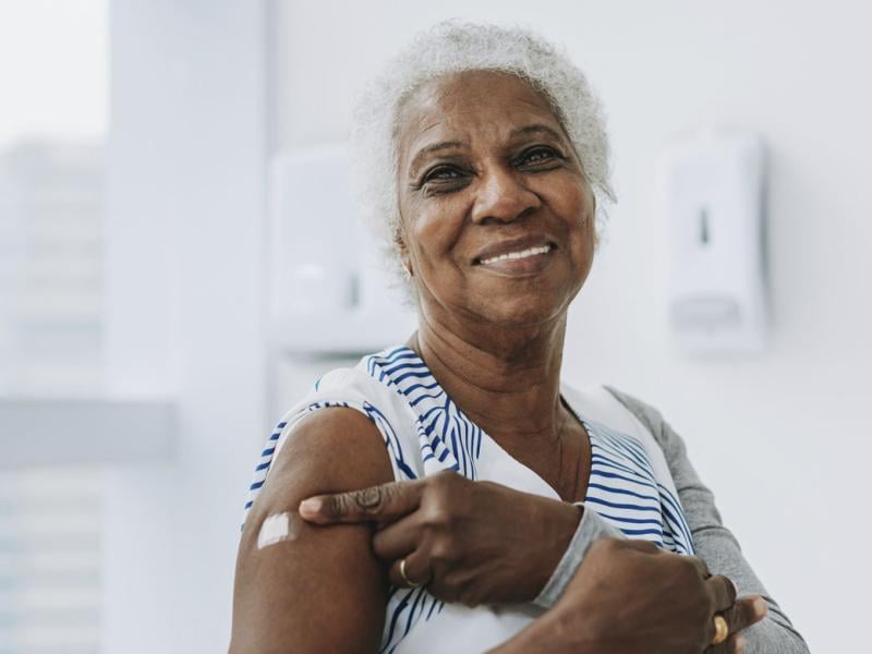 Smiling woman points to bandage on upper arm