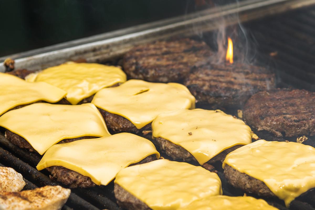A photo of about 10 cheeseburgers cooking on a grill