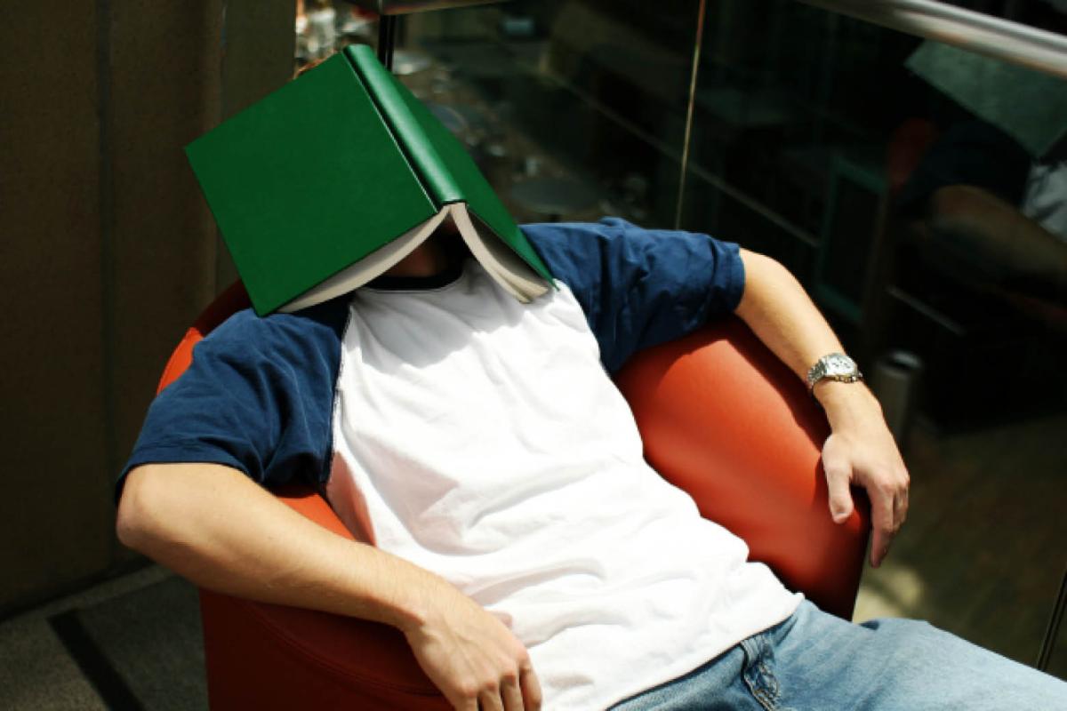 Student reclining in chair with book covering his face