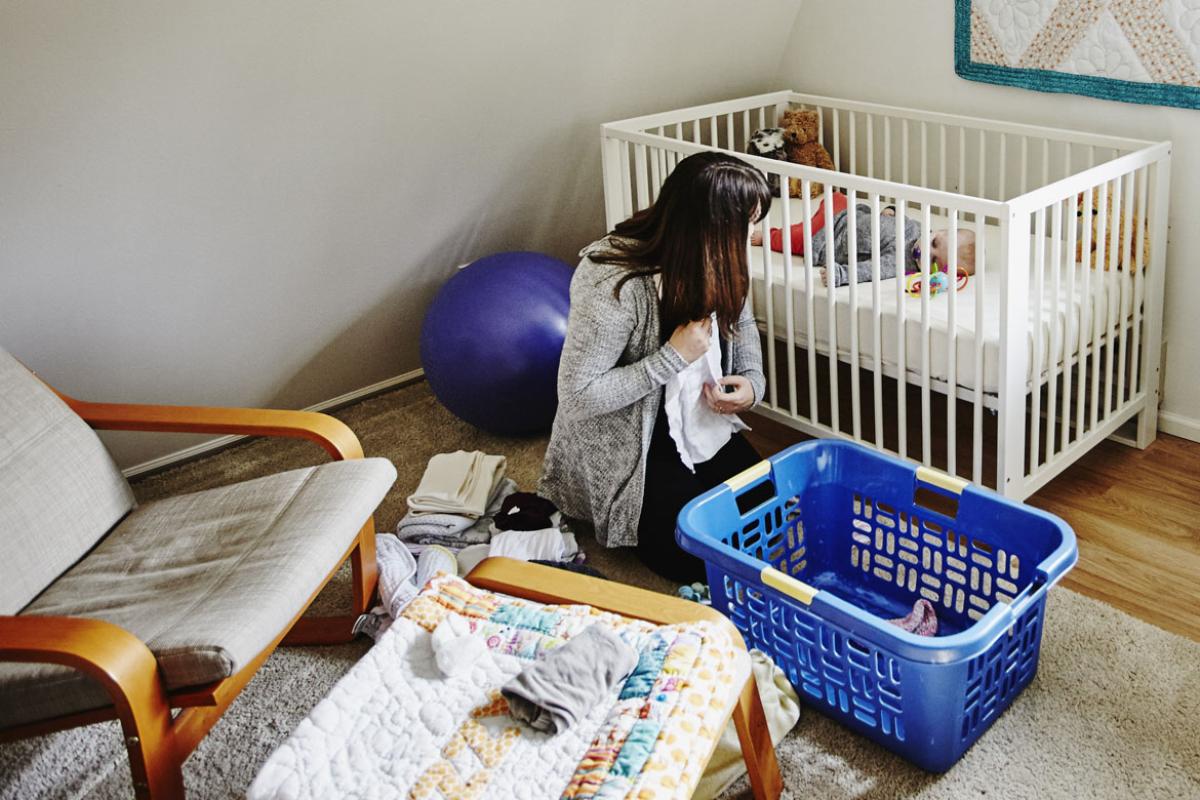 Mother folding clothes while baby sleeps in crib