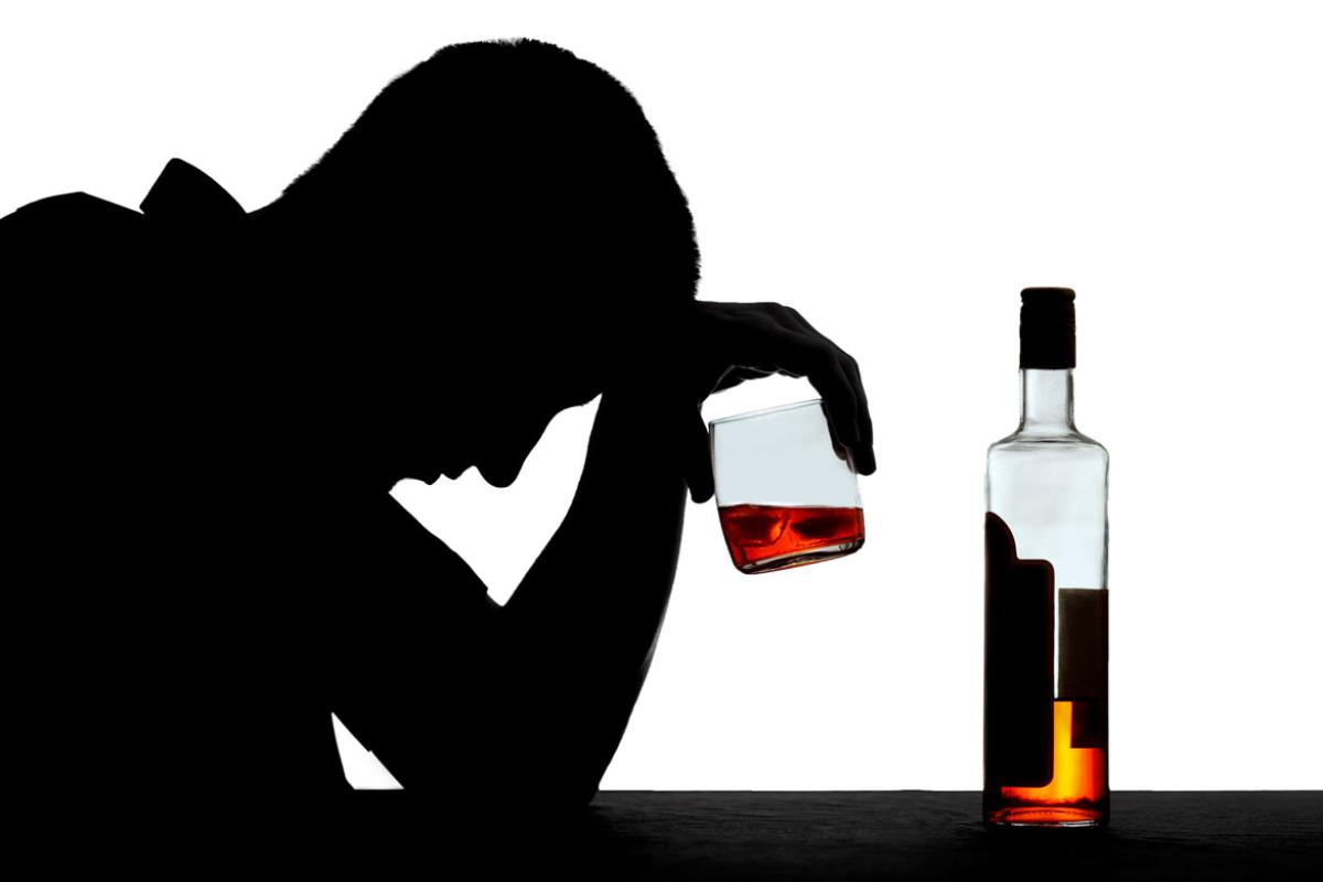 A silhouetted figure holding a glass of alcohol