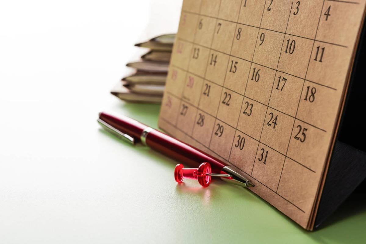 Paper calendar with a red pen and red thumbtack in front of it