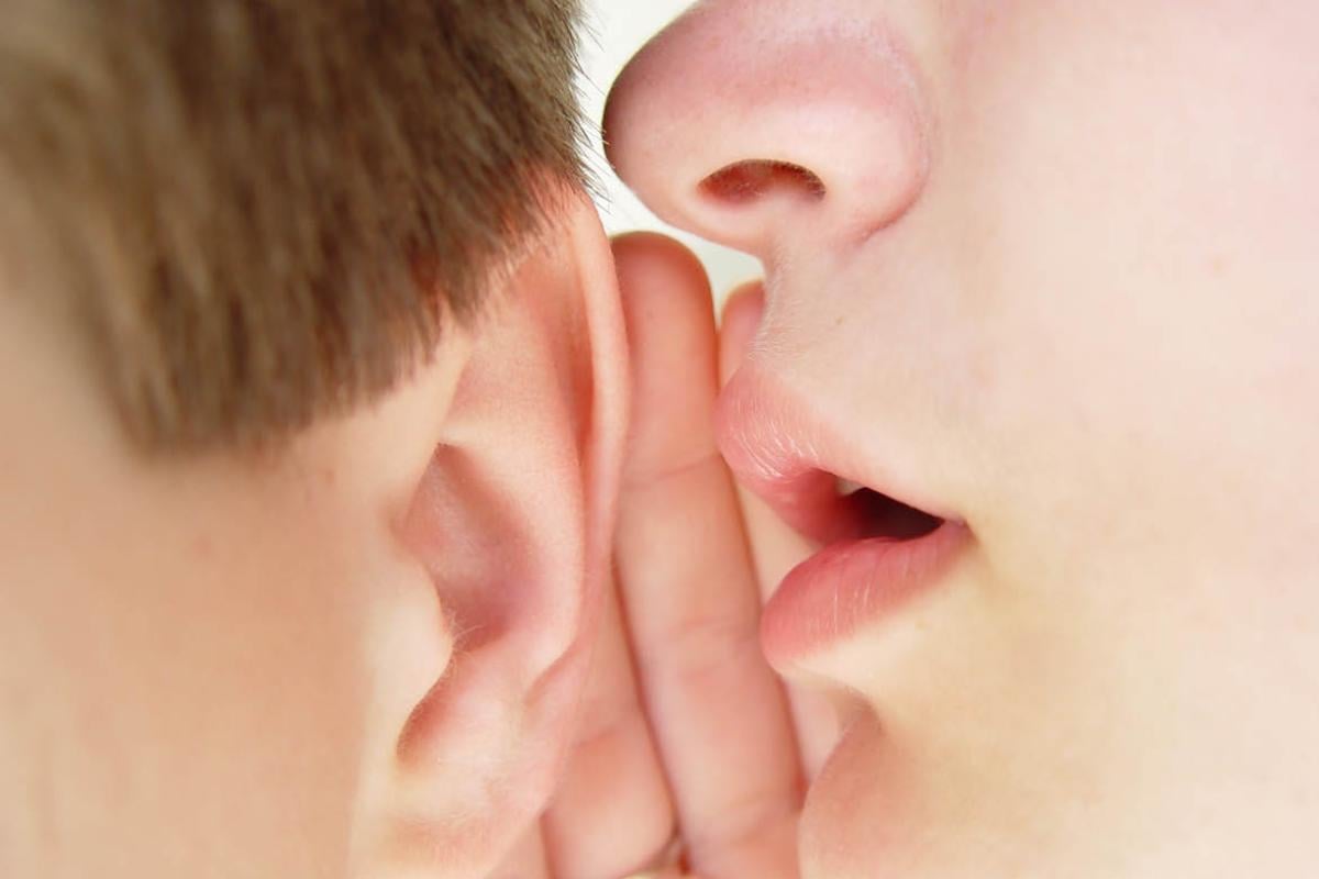 One person speaking into another person's ear
