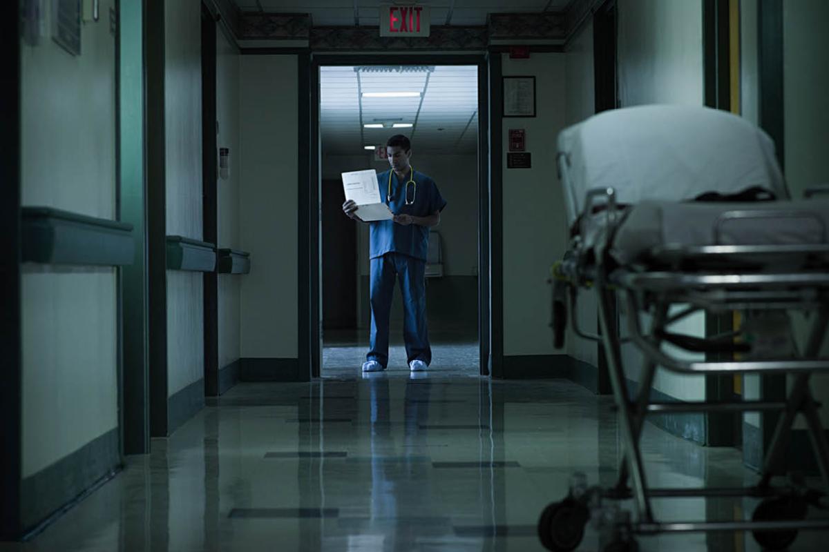 Physician standing in hospital hallway, looking at a chart