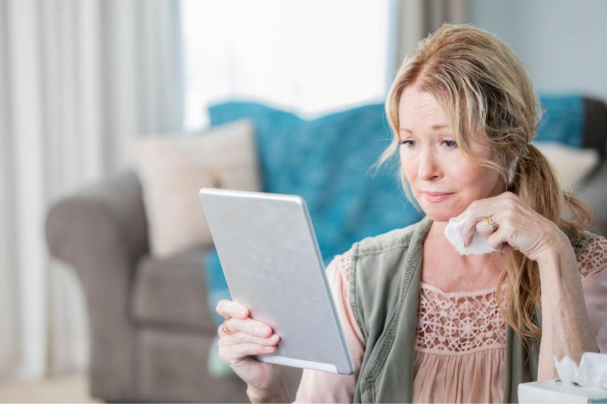 Woman looking at tablet and holding a tissue