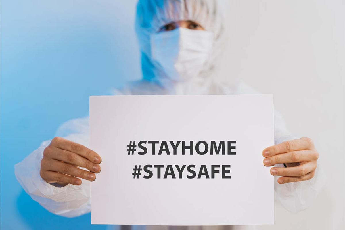 Health care professional holding a "Stay home, Stay safe" sign