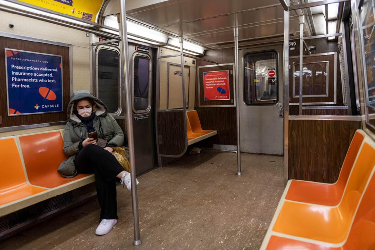 Person in a face mask sitting on an empty subway car