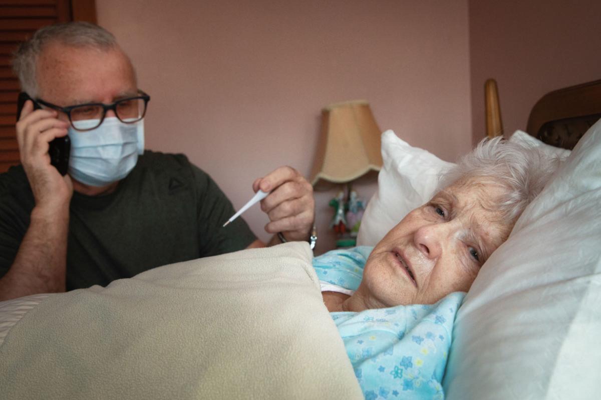 Man with thermometer sitting next to woman lying in bed