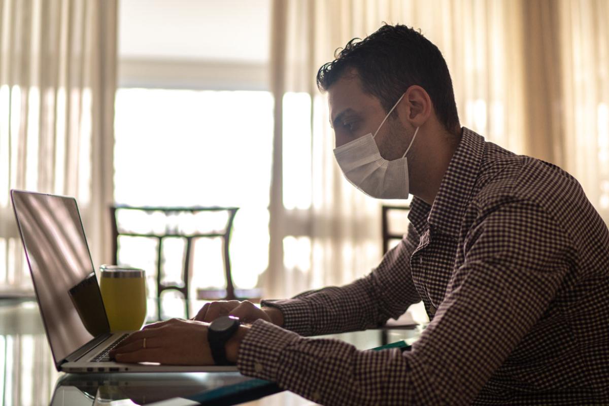 Man wearing facemask and typing on laptop