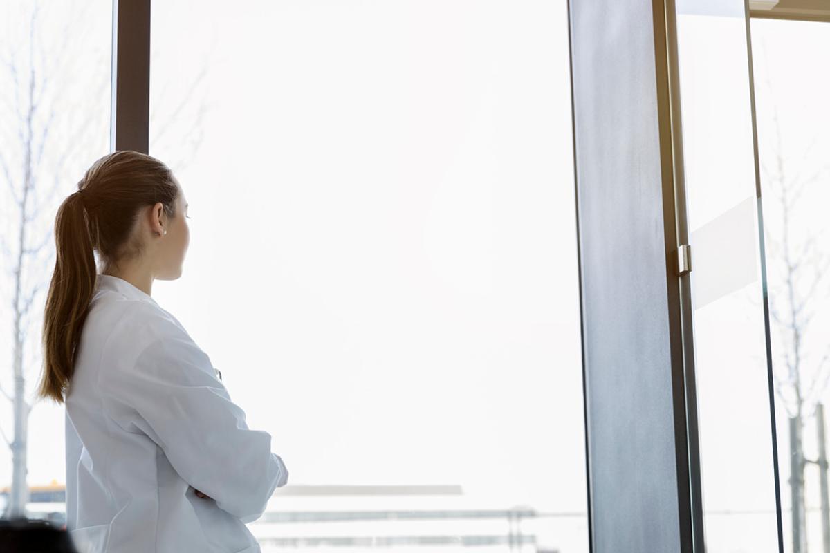 Woman in lab coat looking out window