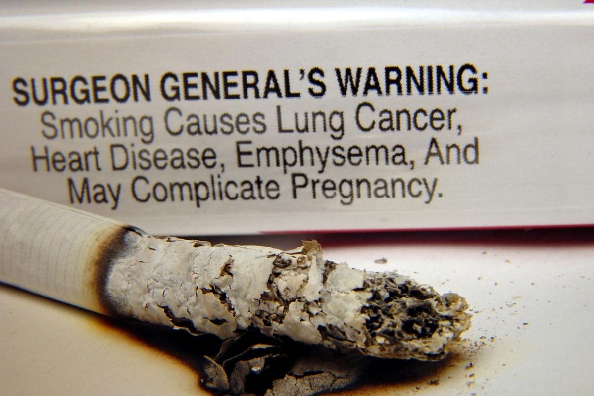 Close-up of a burning cigarette and cigarette pack text-only warning label