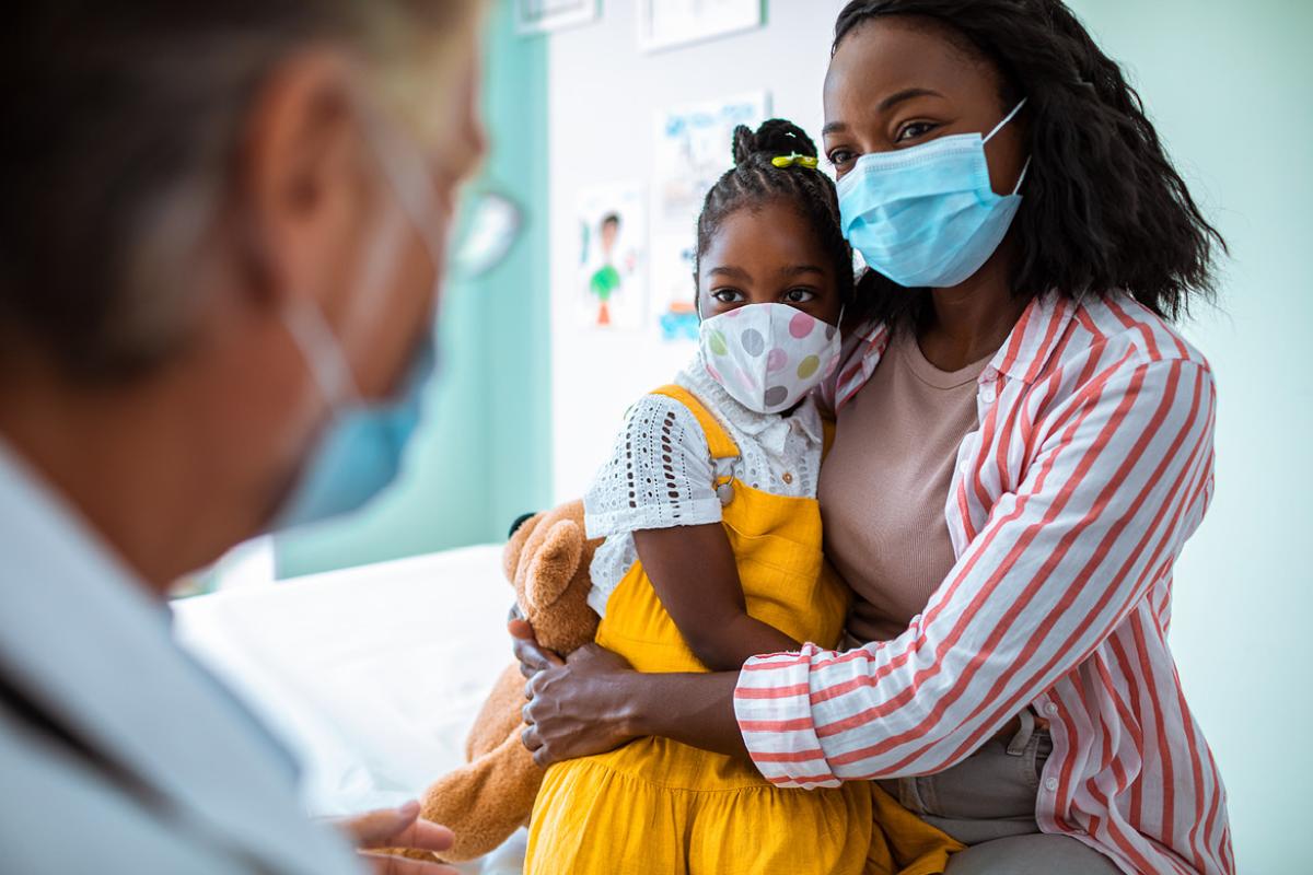 A doctor speaking to an African-American mother and her child, all of them wearing masks.
