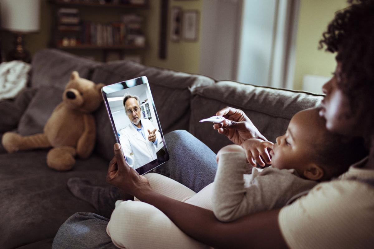 A mother and child sitting on a couch talking to a doctor on a smart pad