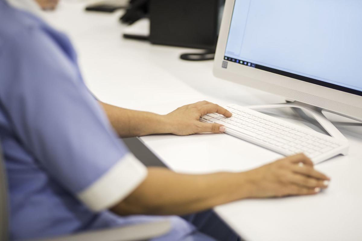 Health care worker at desk typing on keyboard_Tight shot of arms and hands