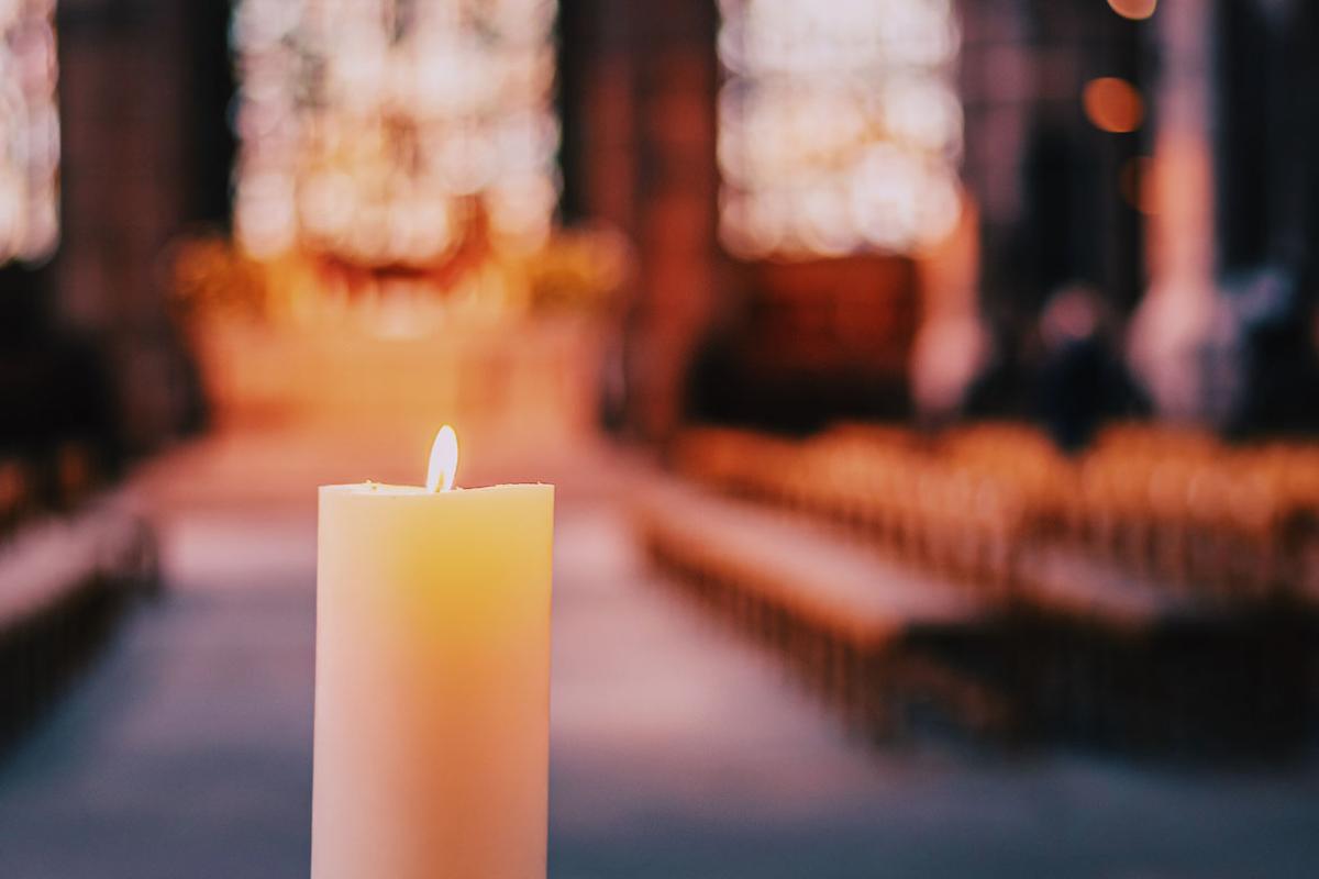 Flickering candle in a church with pews and stained glass windows in background.