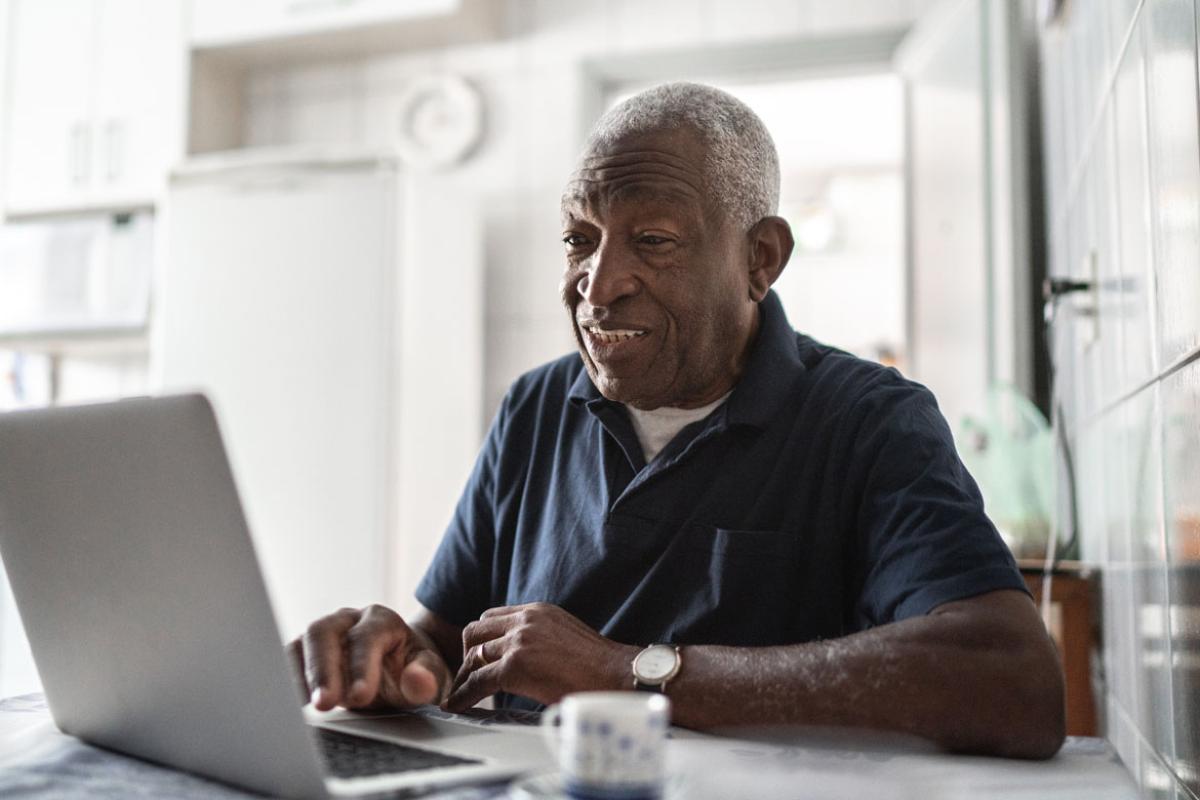 An older African-American man using a laptop computer in his kitchen.