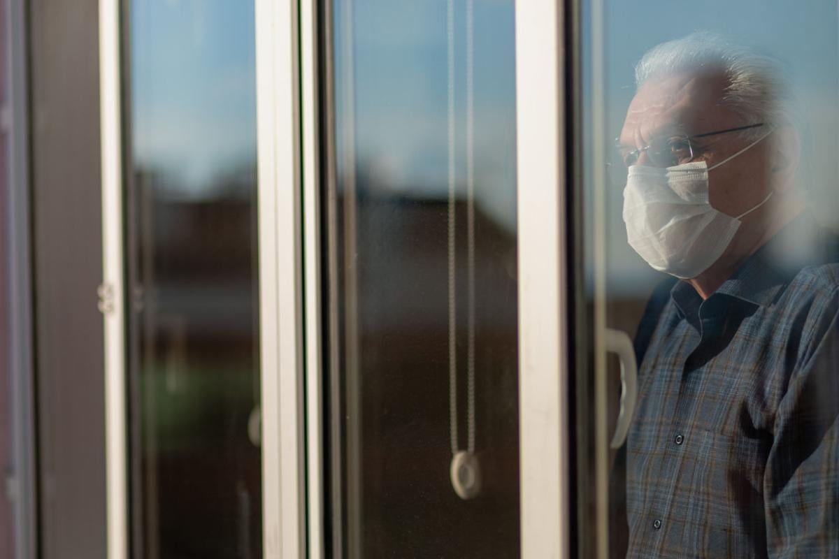 Person in face mask looking out a window