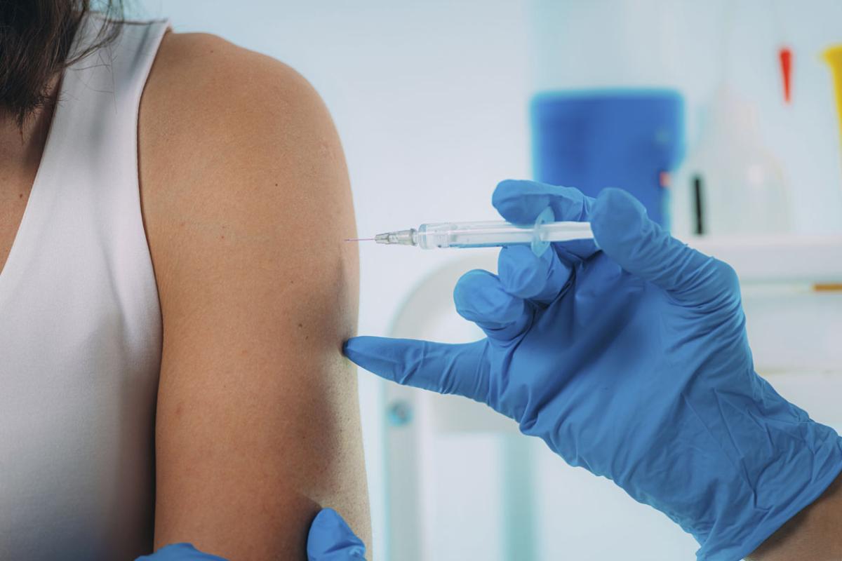 Close-up of a woman's arm and shoulder as she is being given a vaccination by a gloved hand.