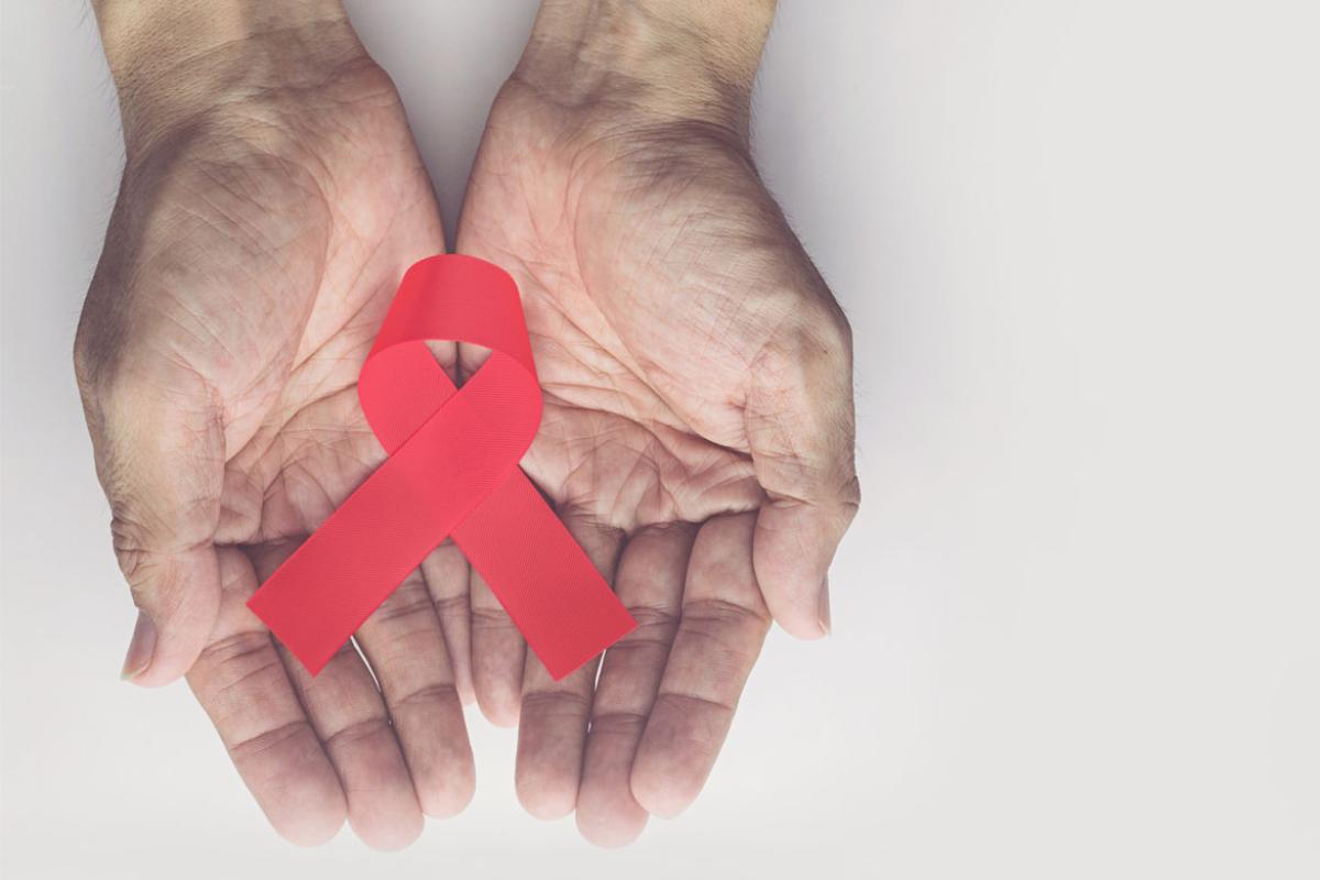 A pair of hands, palms up, holding a red AIDS ribbon against a white background.