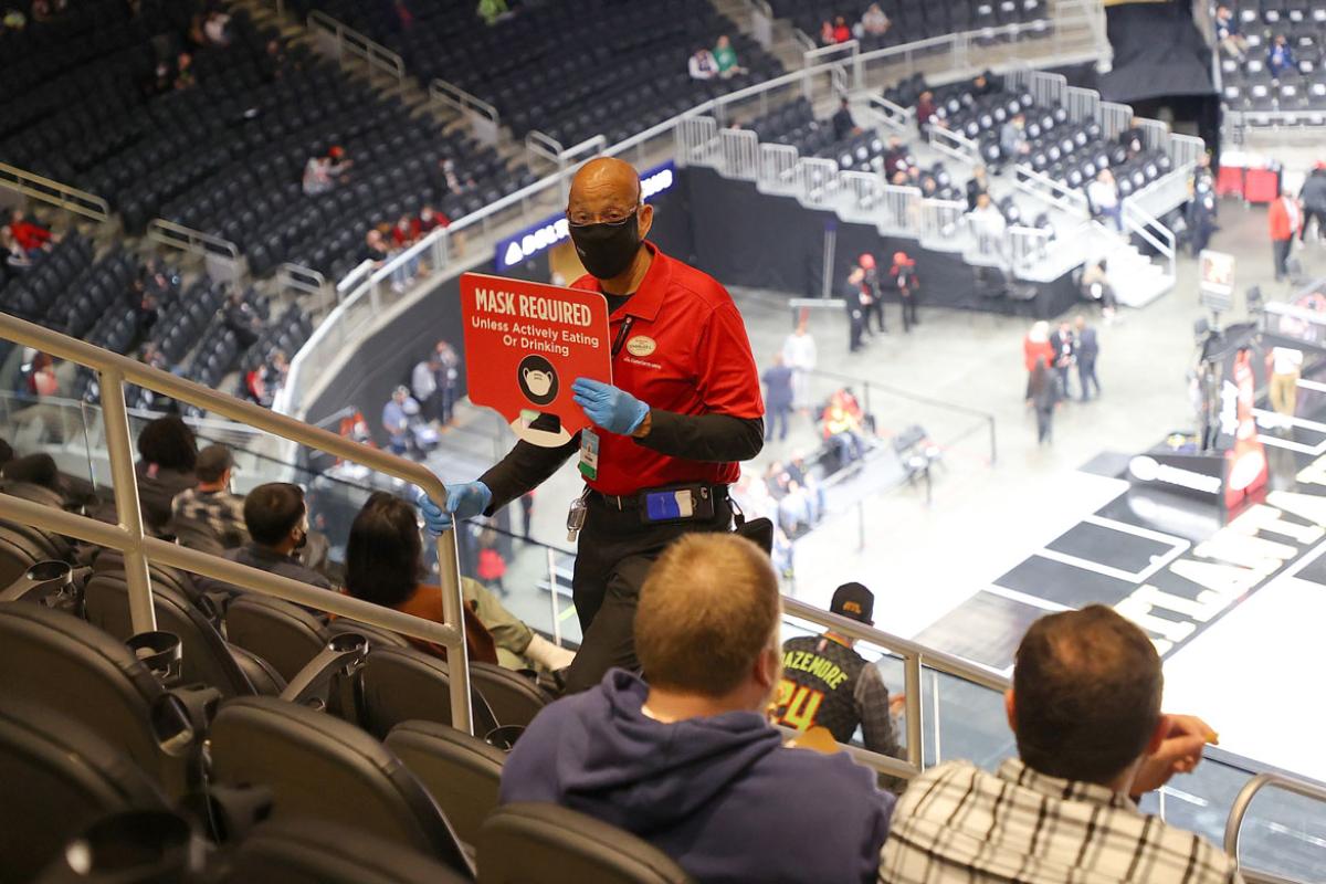 Seating in a sports arena, with a couple being shown a signing reading masks required by an usher.