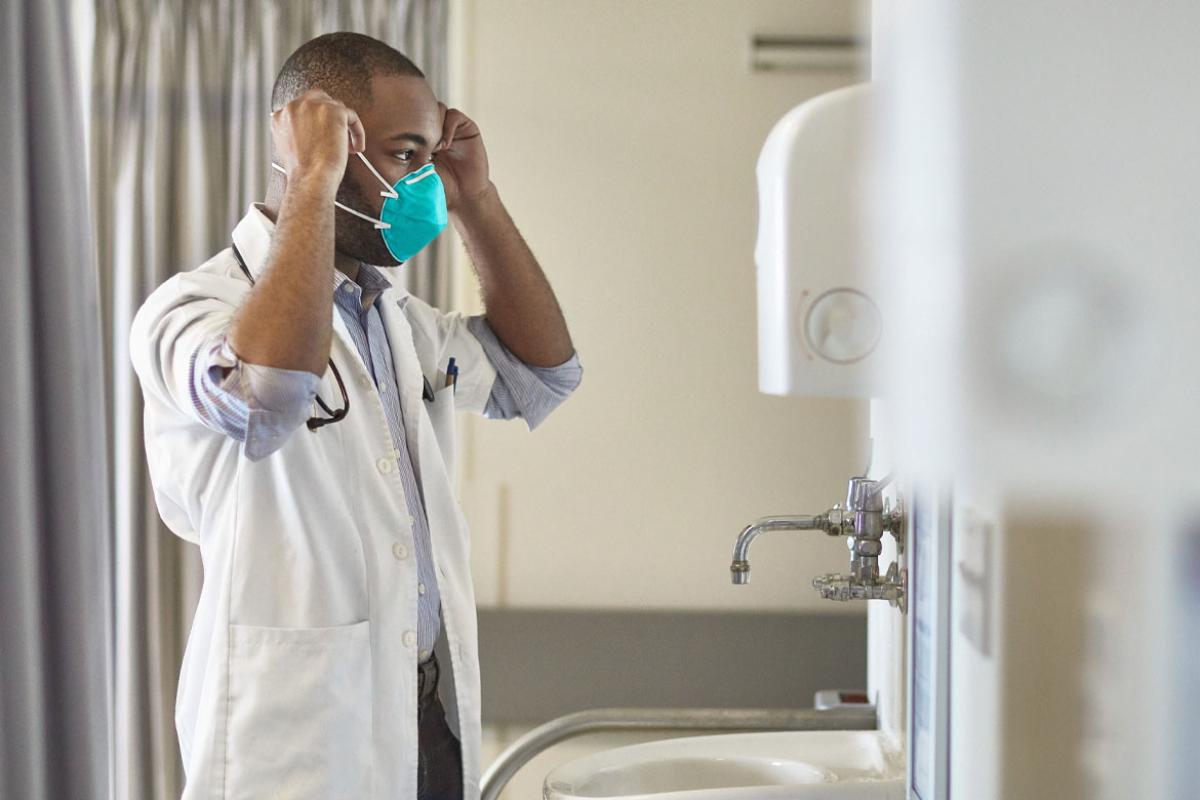 Physician adjusting a mask in front of a mirror and sink