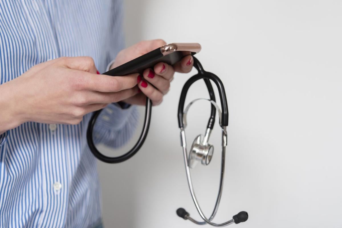 Tight shot of person using a cell phone while holding a stethoscope in the left hand.
