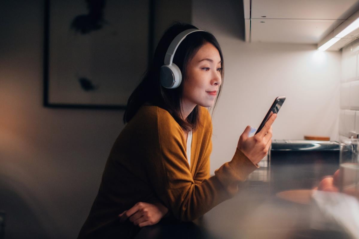 Young woman wearing bluetooth headphones and listening to music or a podcast on a cellphone.
