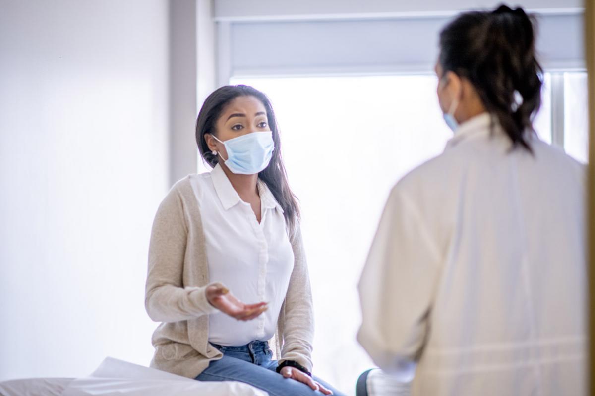Female patient and physician talking during a patient visit, both wearing masks