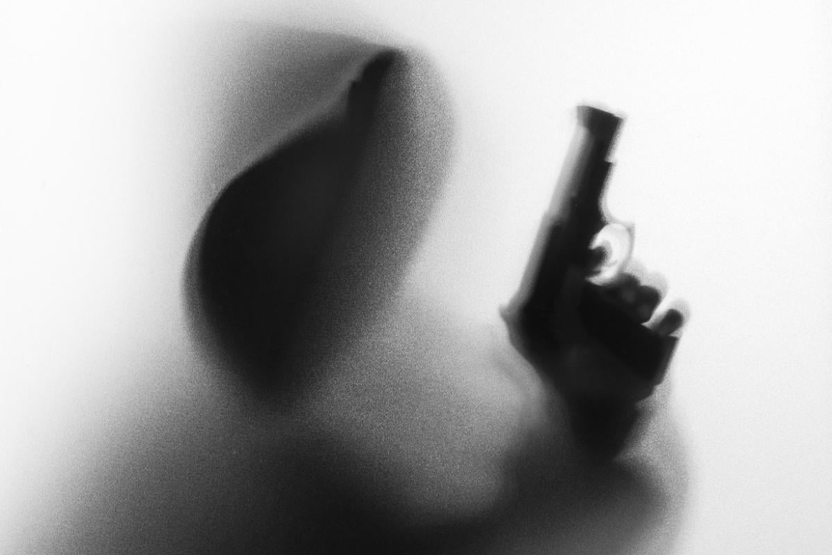 Image of a person's face in shadow holding a gun