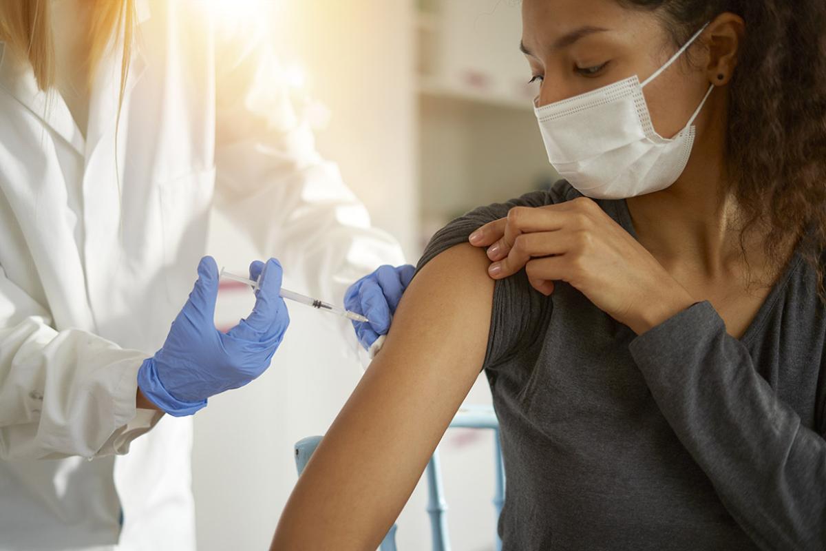 Woman wearing a mask and rolling up her sleeve to get a vaccination from a physician