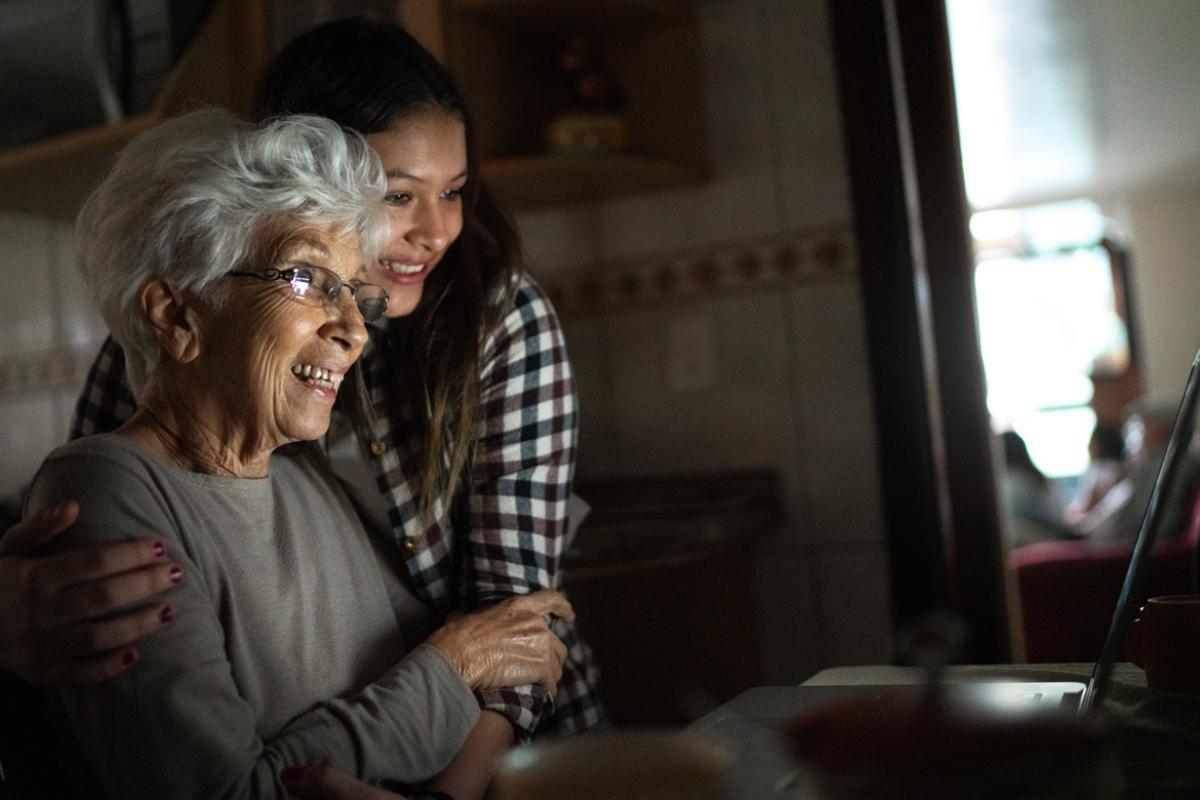 A grandmother and granddaughter viewing a laptop screen and embracing
