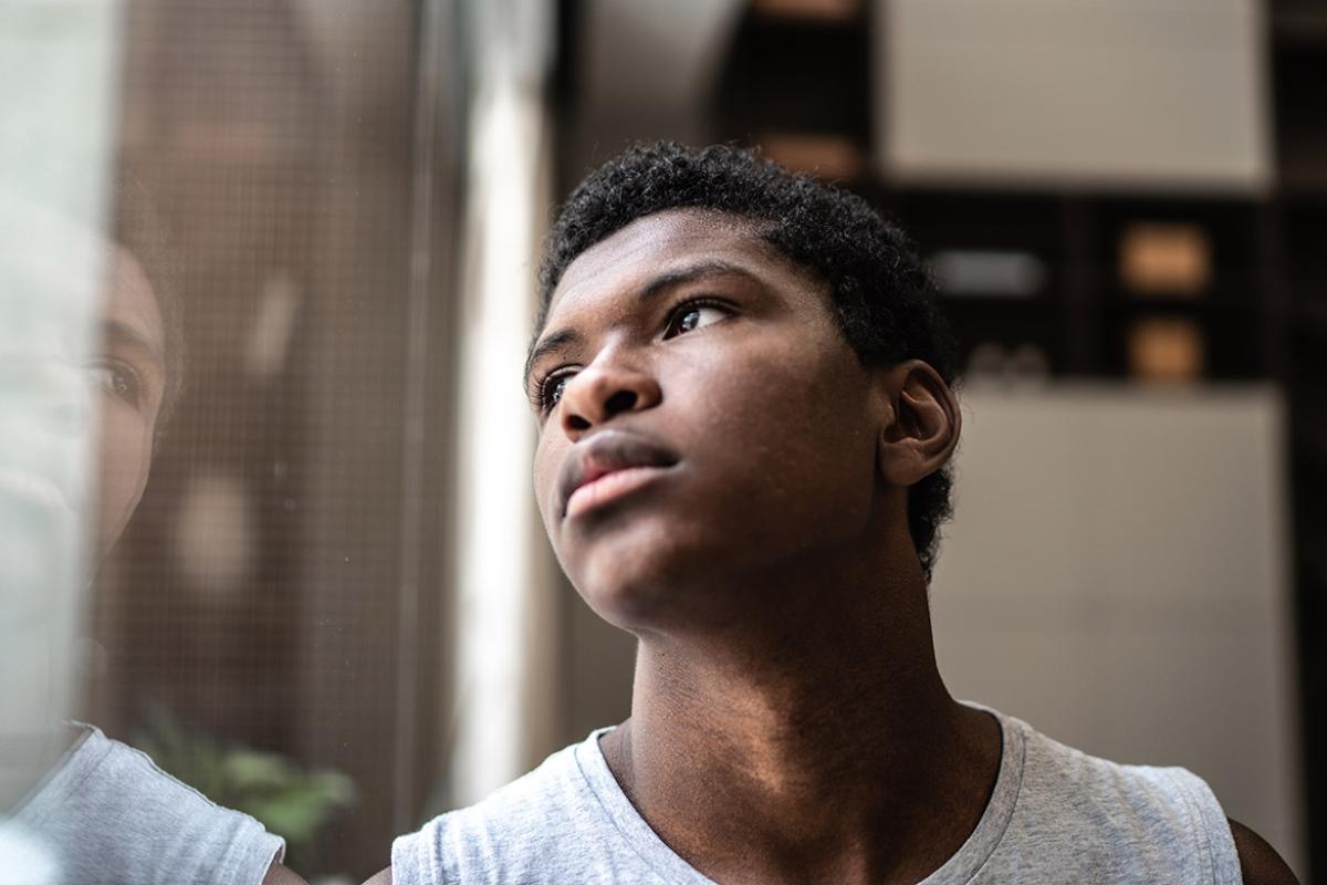Young teen man looking through window glass