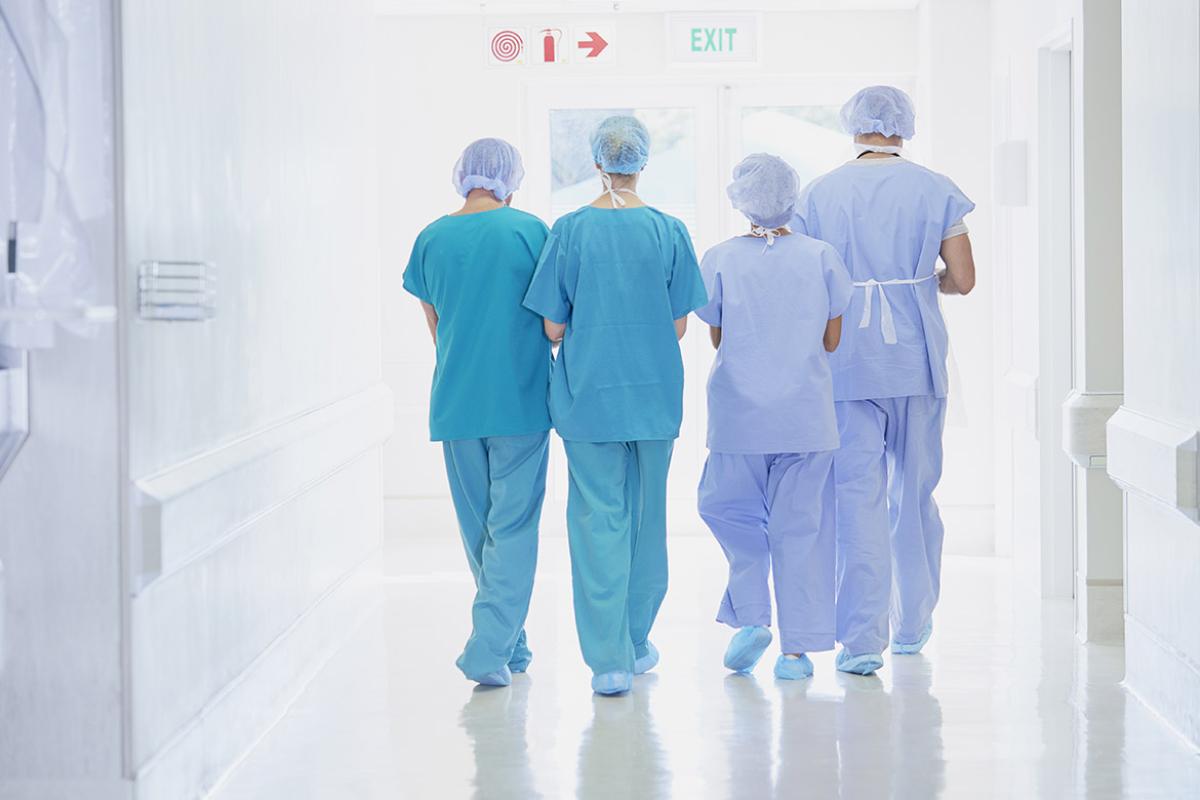 View from the back of four health care professionals wearing scrubs exiting an operating room