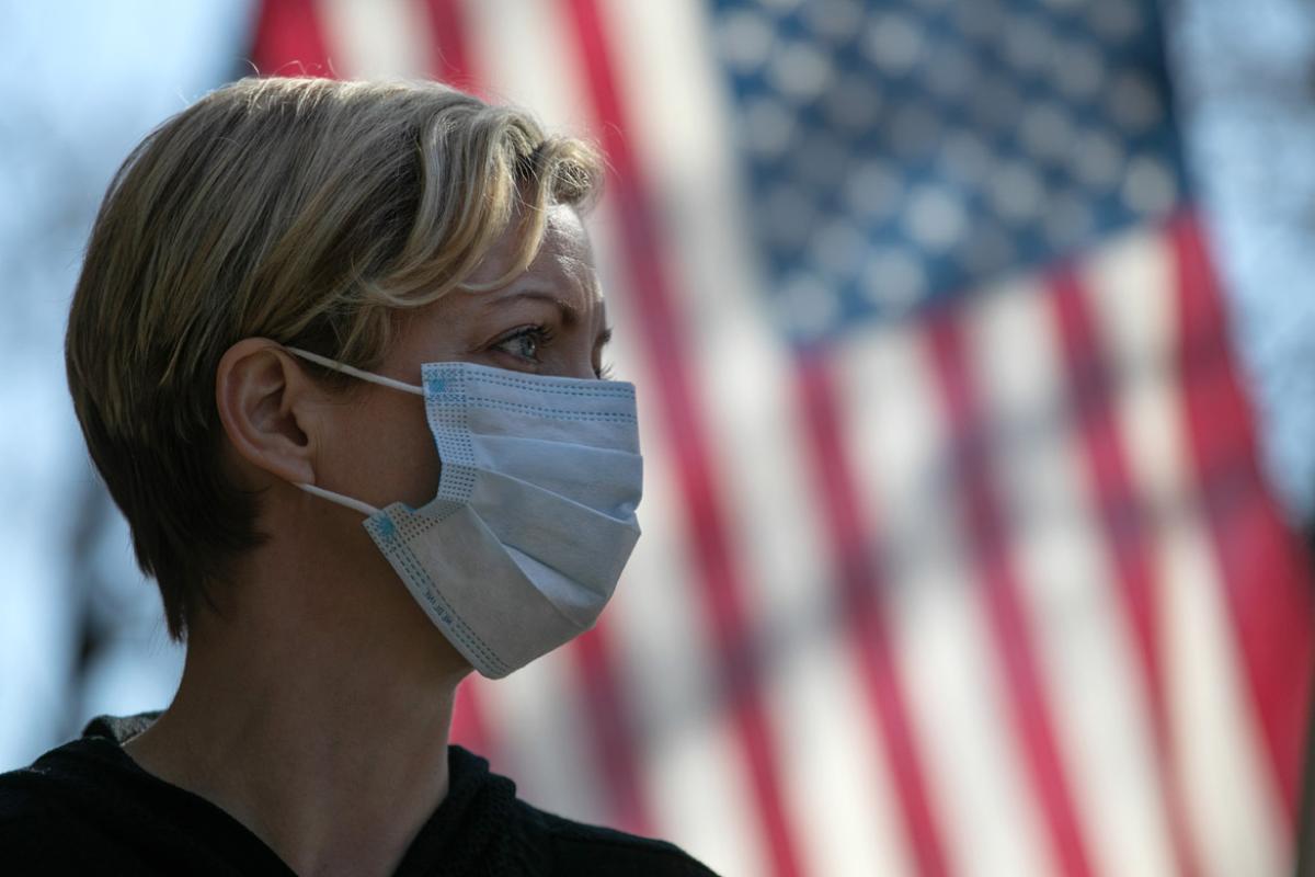Tight shot of woman wearing a face mask with the U.S. flag in the background