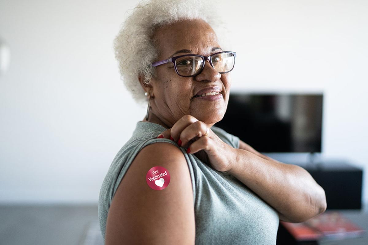 Smiling person showing their arm with a "Get Vaccinated" sticker