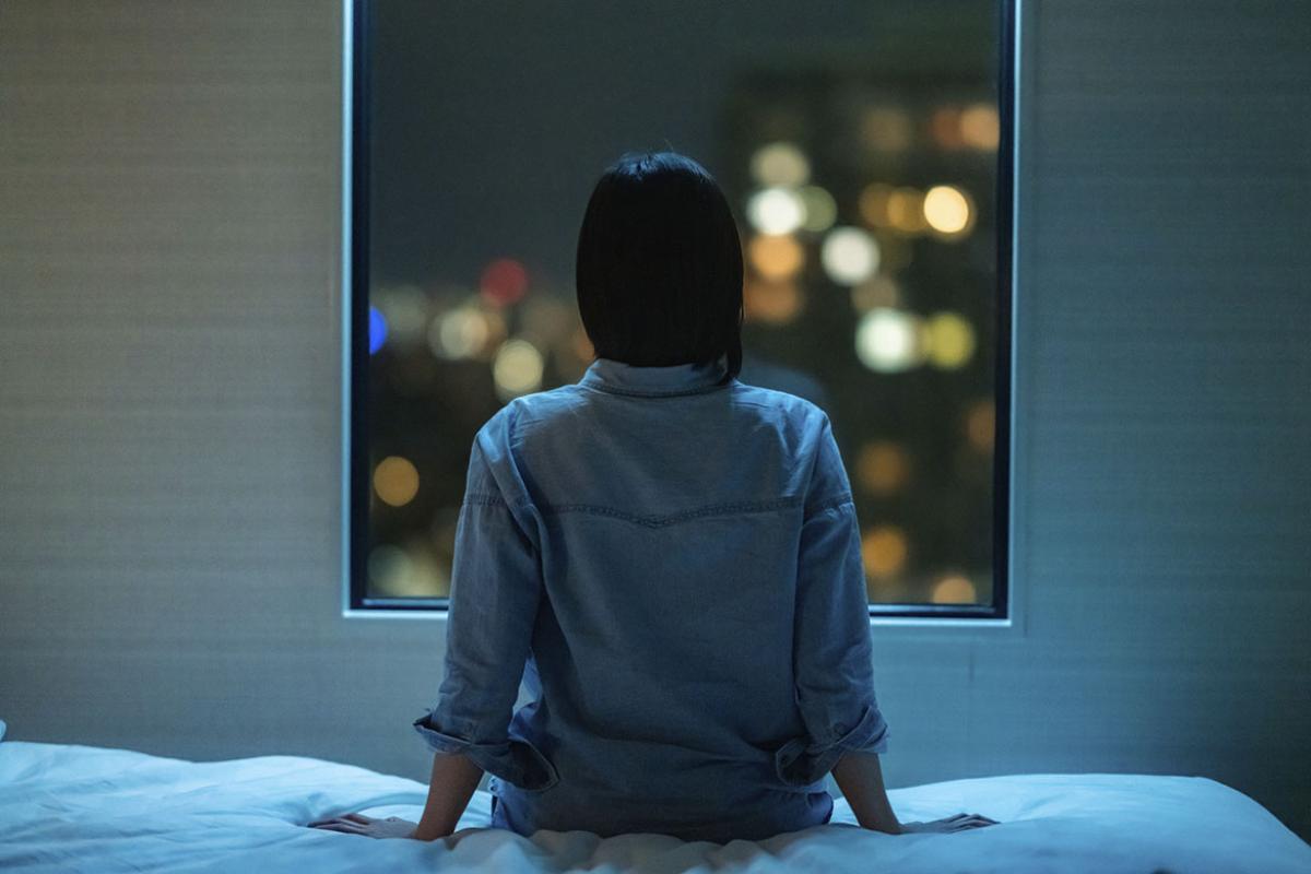 Person sitting on a bed and looking out a window