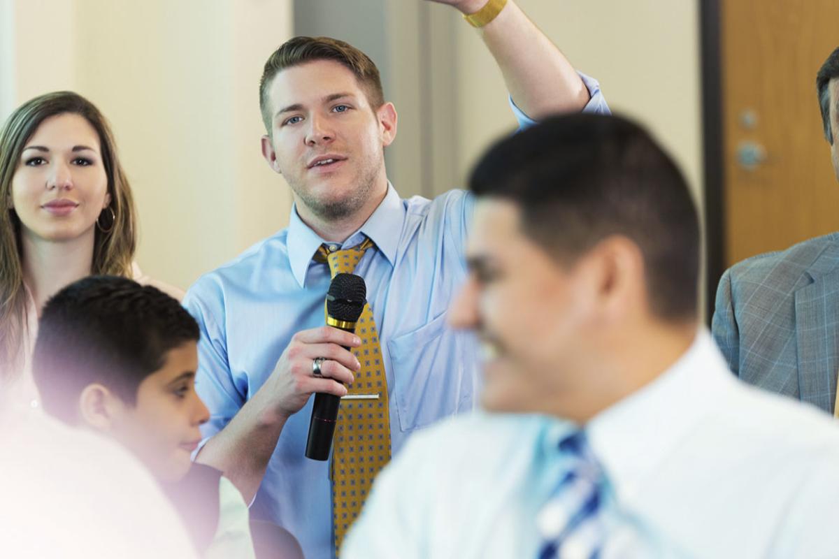 Person holding a microphone raises hand during meeting