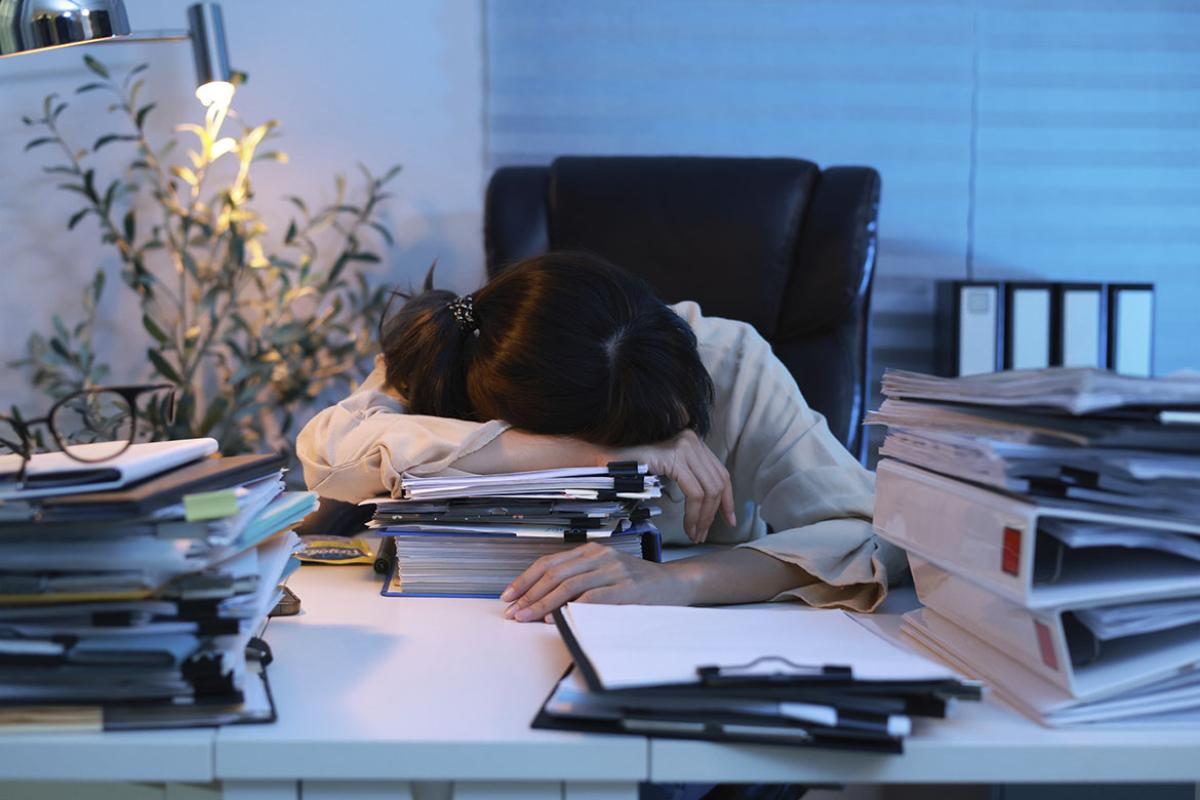 Person at desk sleeping on a stack of documents