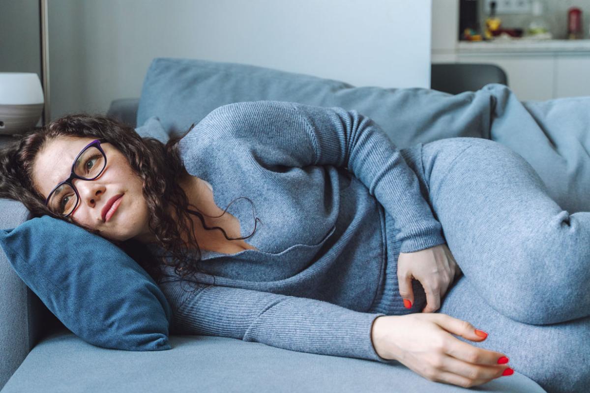 Woman lying on sofa and hand cradling abdomen
