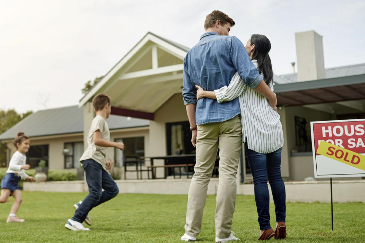 Smiling family in front of a house with a sold sign