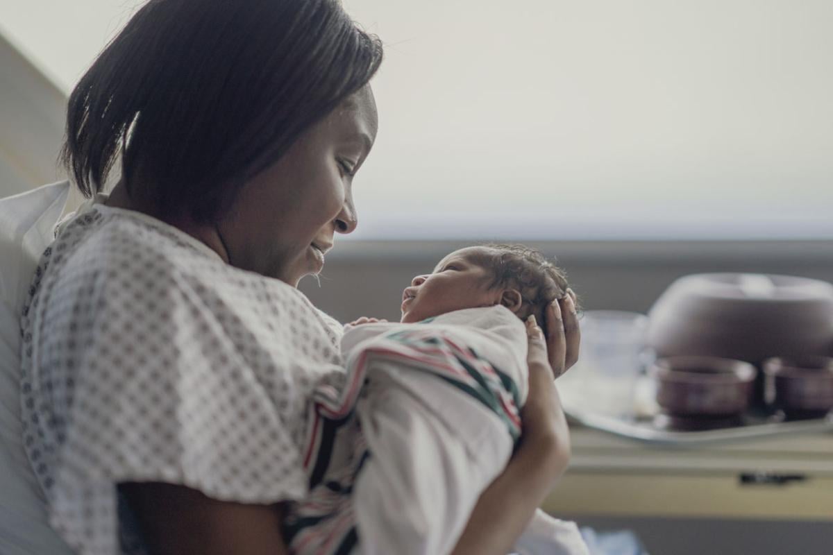 A mother holds her newborn baby as she sits up in a hospital bed