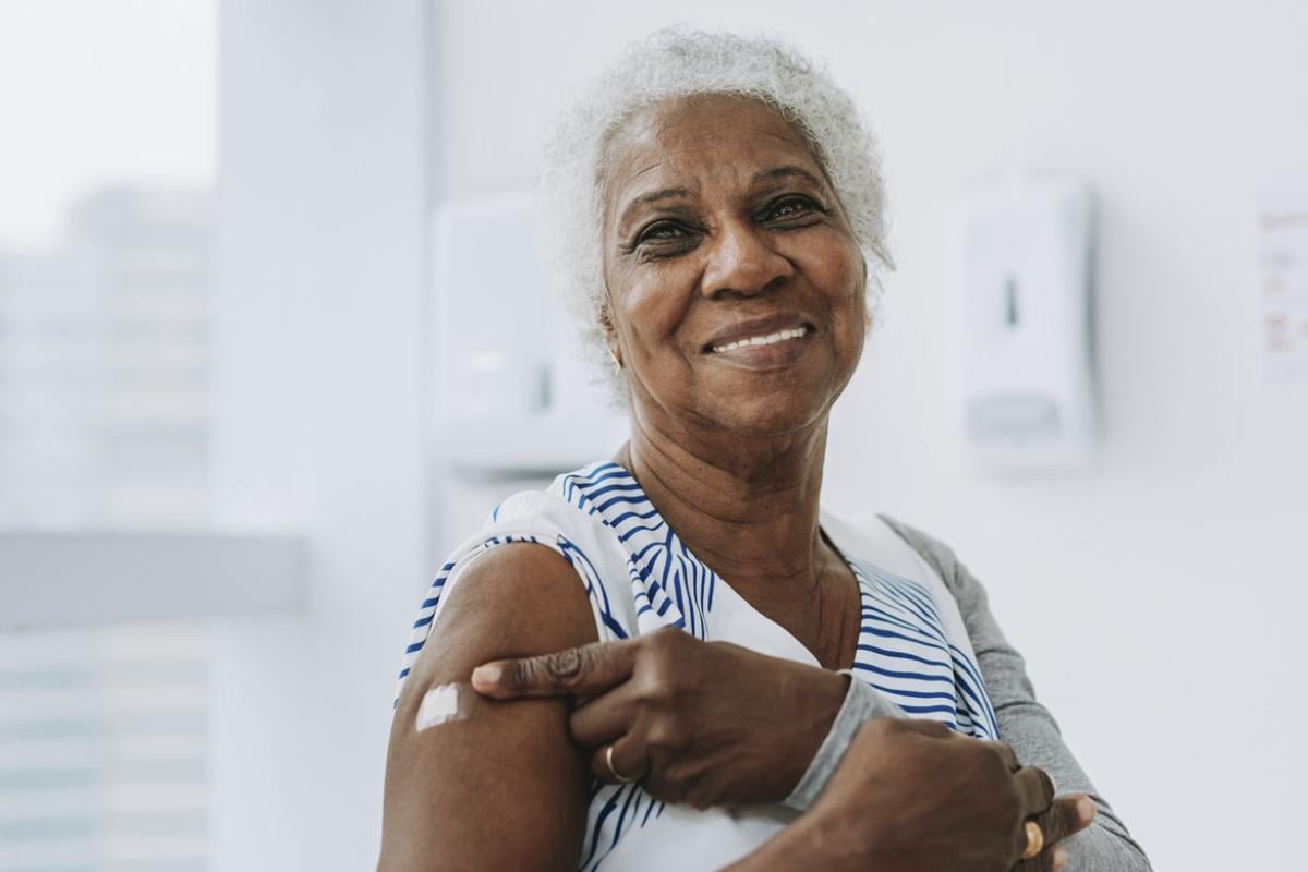 Smiling woman points to bandage on upper arm