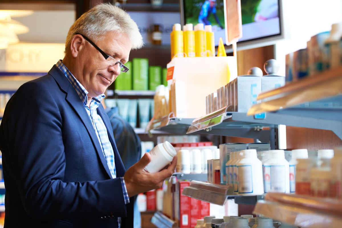 Man in pharmacy looking at medicine bottle.