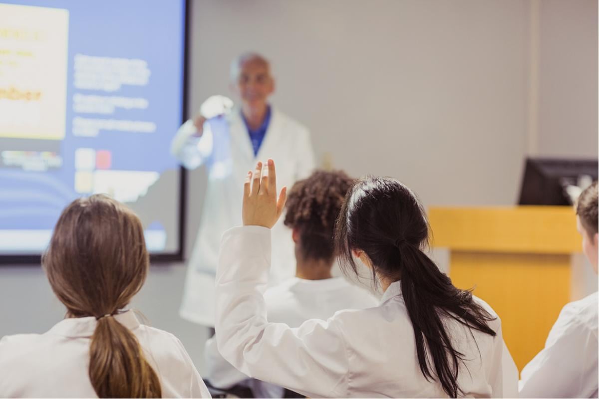 Student in medical classroom raises hand to answer instructors question.
