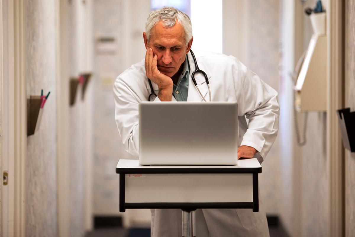 Physician with chin in hand looking at a laptop.